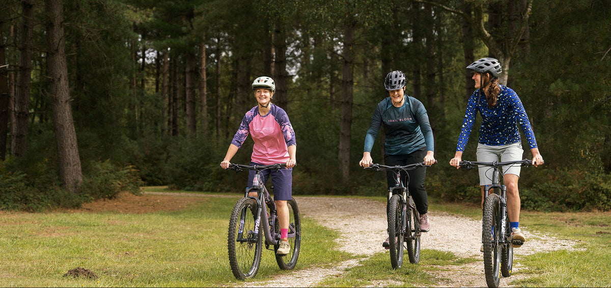 Three people riding bicycles on a trail through a forest in ladies MTB jersey